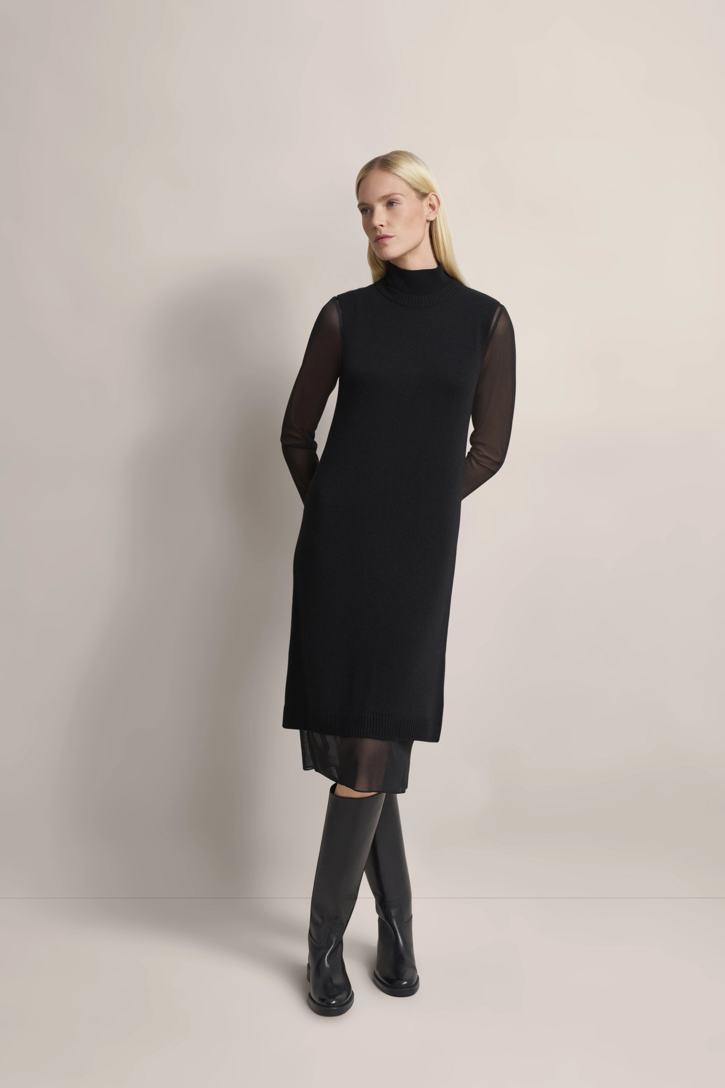 Schwarzes bugatti Kleid mit transparenten Ärmeln, Model stehend mit Händen in den Taschen.