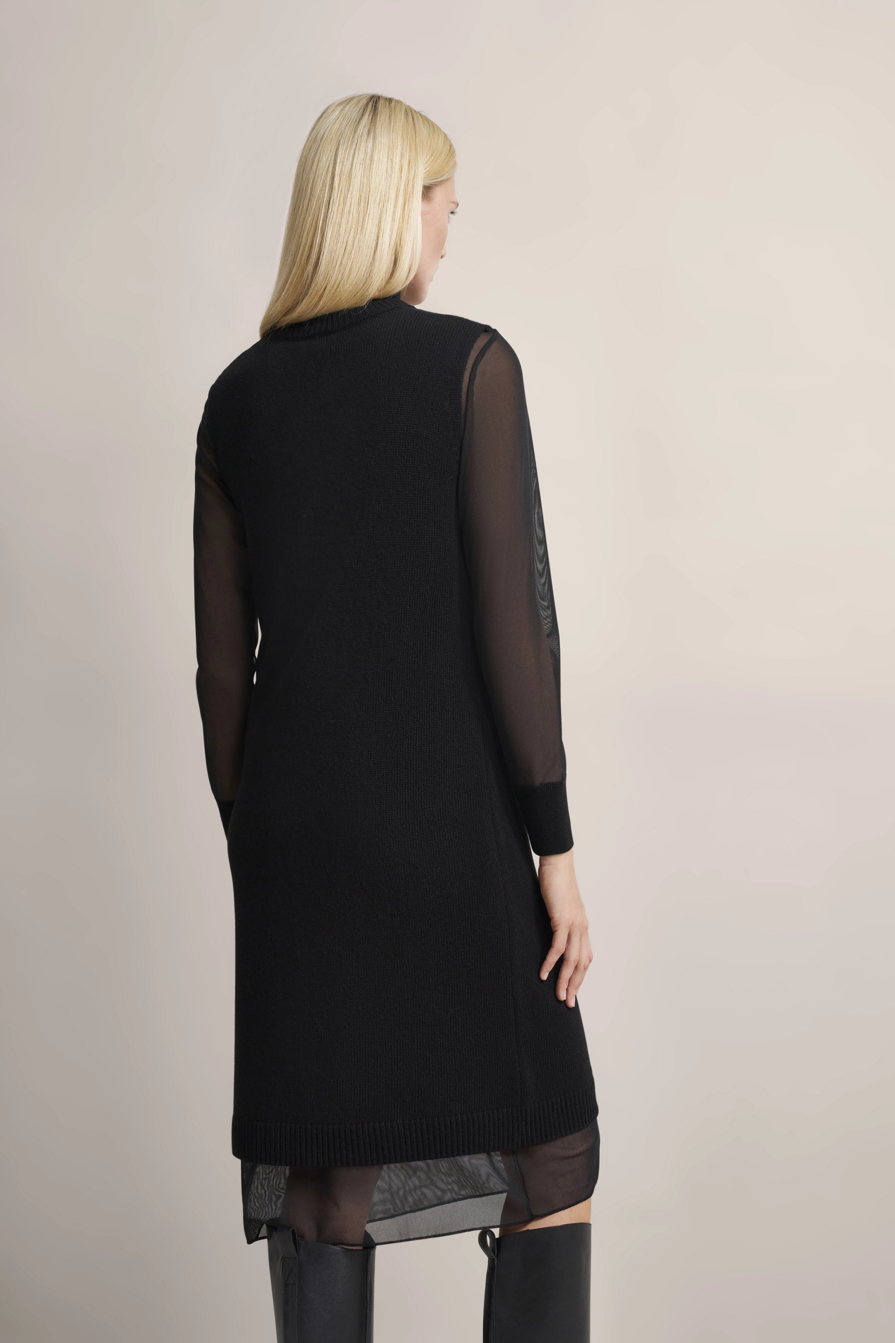 Model trägt schwarzes bugatti Kleid mit transparenten Ärmeln, Rückenansicht, entspannte Pose.