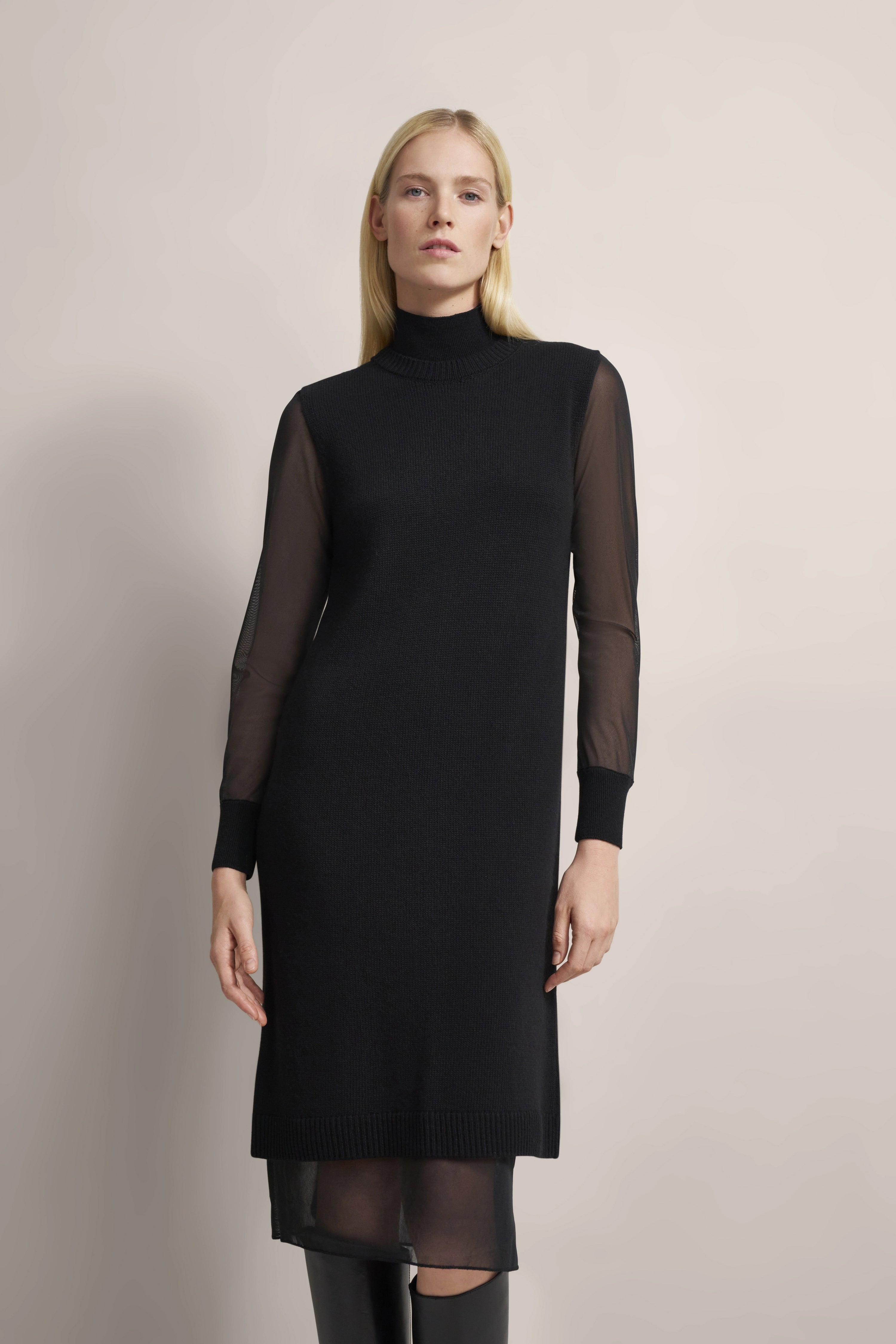 Black bugatti dress with sheer sleeves, model facing forward in a relaxed pose.