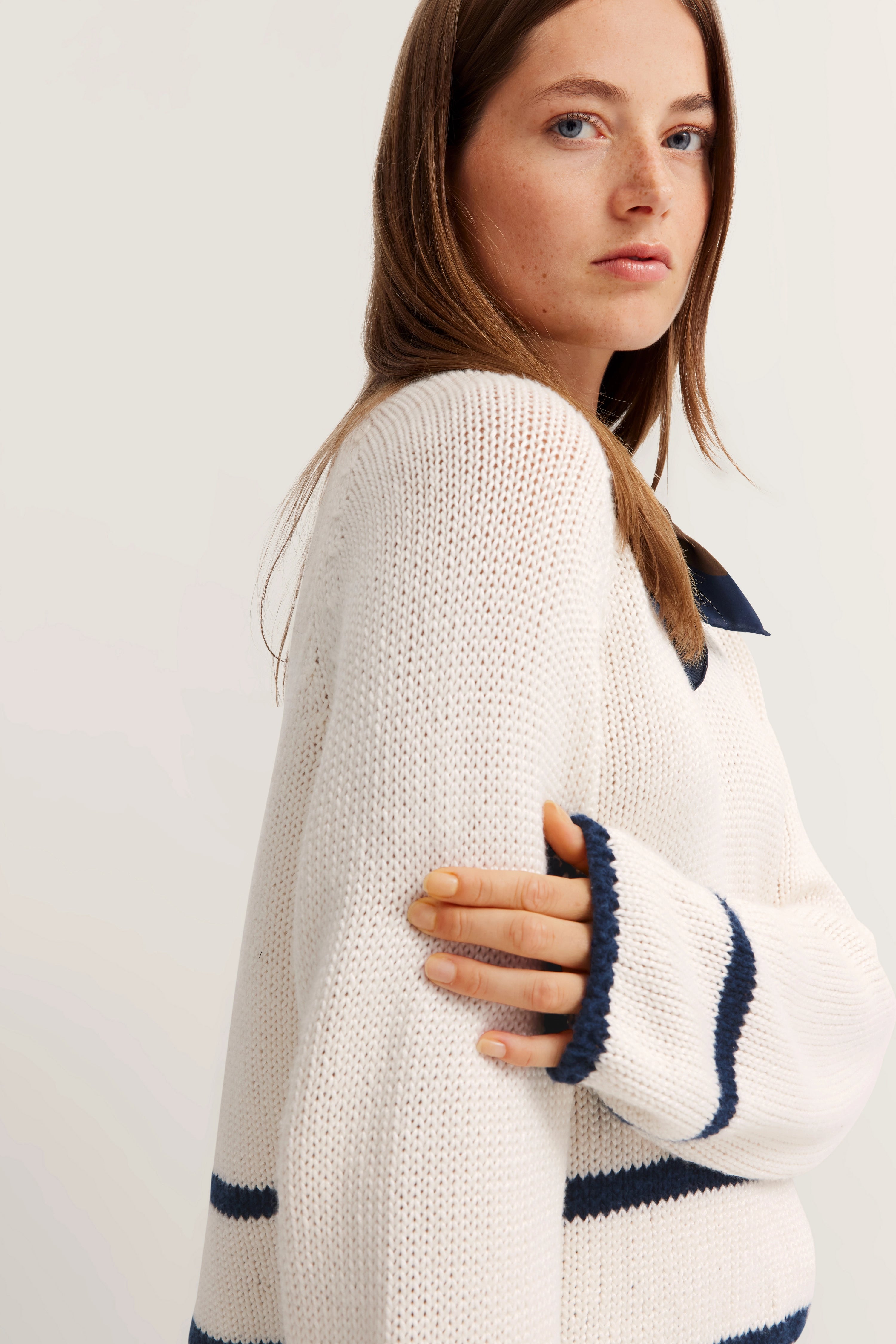 Model in weißem Strickpullover mit blauen Streifen, Halbprofil-Pose.