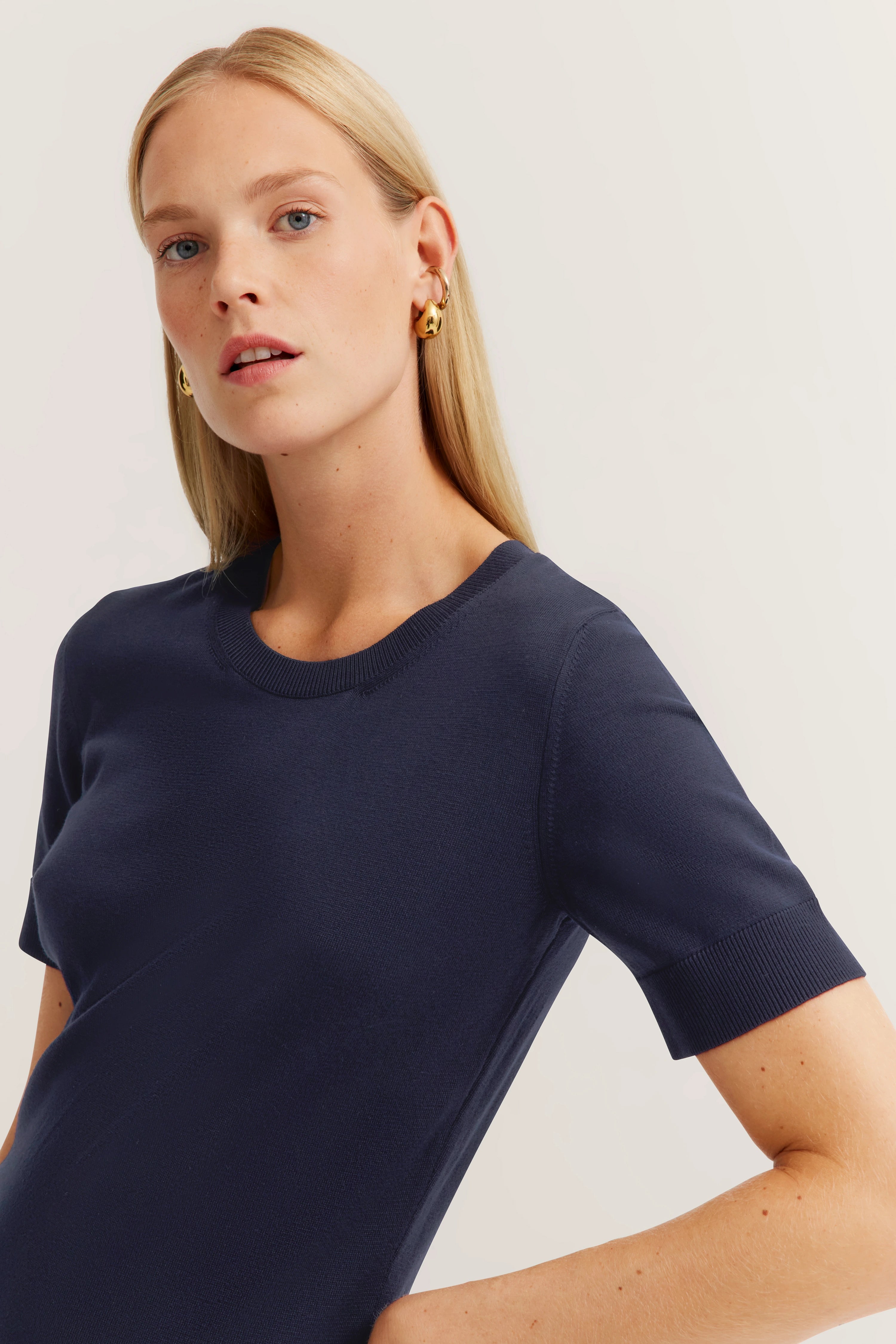 Navy blue bugatti top, short-sleeved, model tilts head left, elegant look.